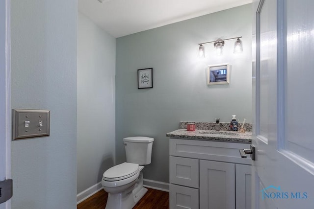 half bath featuring toilet, baseboards, wood finished floors, and vanity