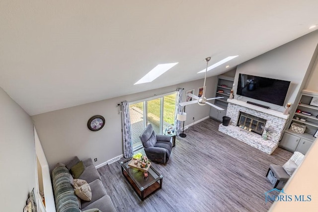 living room with lofted ceiling with skylight, baseboards, wood finished floors, and a stone fireplace