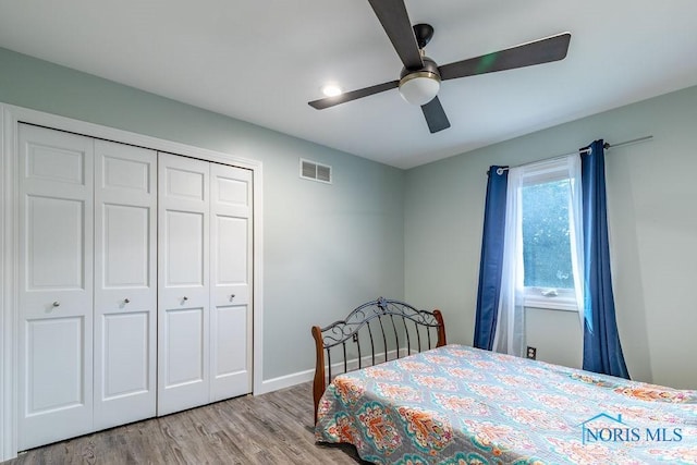 bedroom featuring wood finished floors, visible vents, baseboards, a ceiling fan, and a closet