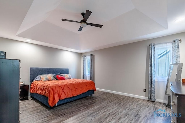 bedroom featuring ceiling fan, recessed lighting, wood finished floors, baseboards, and a tray ceiling