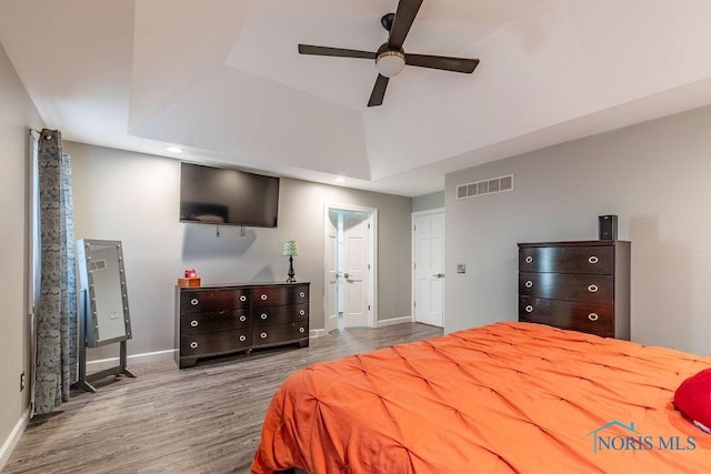 bedroom featuring baseboards, visible vents, ceiling fan, wood finished floors, and a tray ceiling