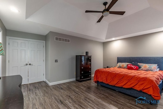 bedroom with a tray ceiling, wood finished floors, visible vents, and baseboards