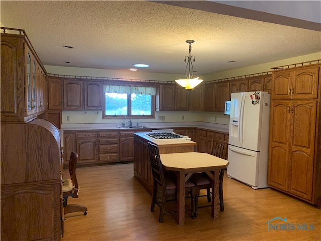 kitchen featuring white fridge with ice dispenser, gas stovetop, light hardwood / wood-style flooring, sink, and decorative light fixtures