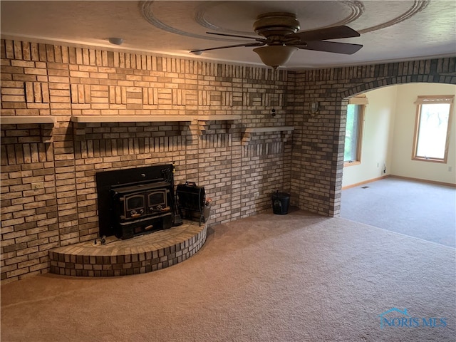 unfurnished living room featuring ceiling fan, a wood stove, brick wall, and carpet