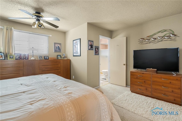 bedroom featuring ceiling fan, a textured ceiling, light carpet, and ensuite bath