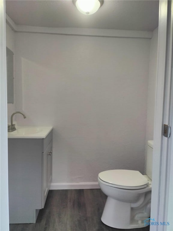 half bath with vanity, wood finished floors, toilet, and baseboards