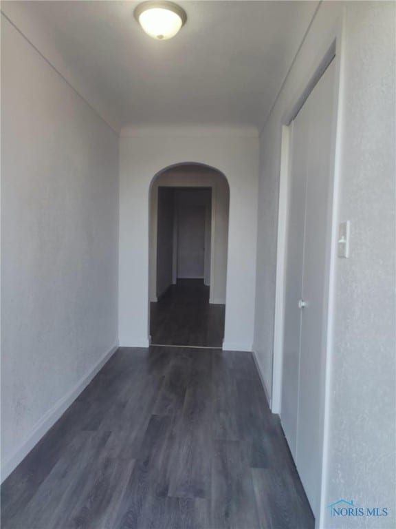 corridor featuring dark wood-style floors, arched walkways, and baseboards