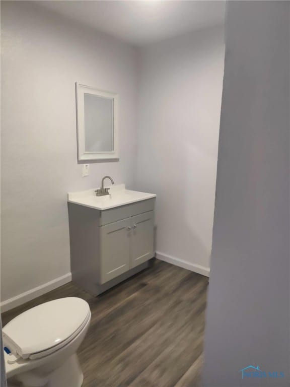 bathroom with toilet, wood finished floors, vanity, and baseboards