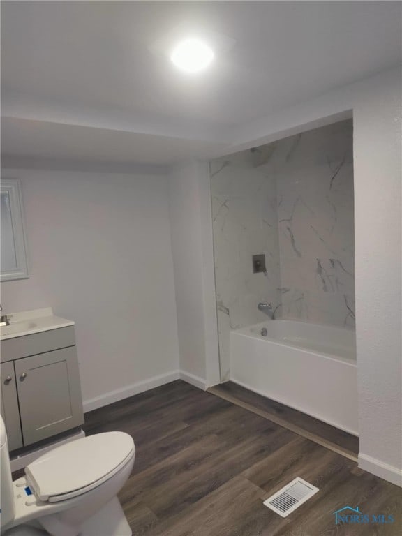 full bathroom featuring wood-type flooring, vanity, tiled shower / bath, and toilet