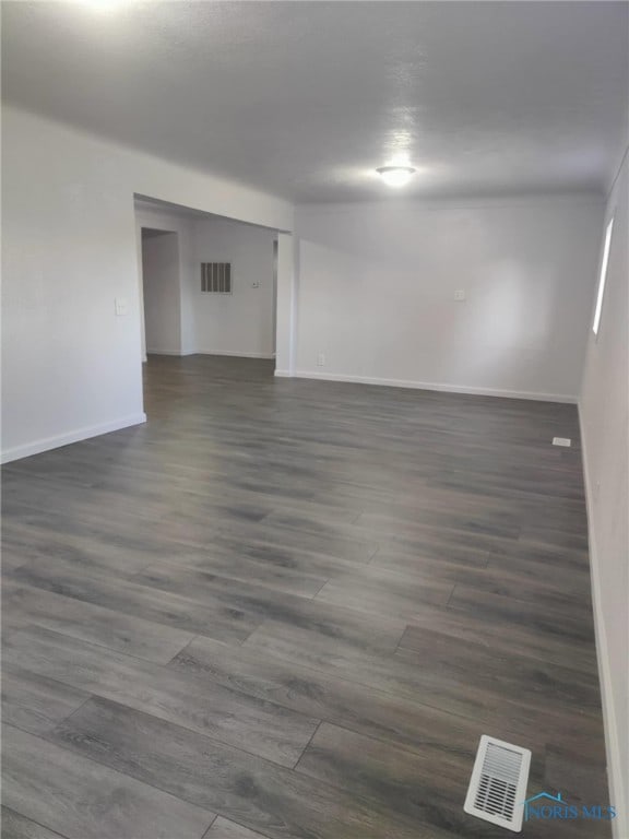 empty room featuring dark wood finished floors, visible vents, and baseboards