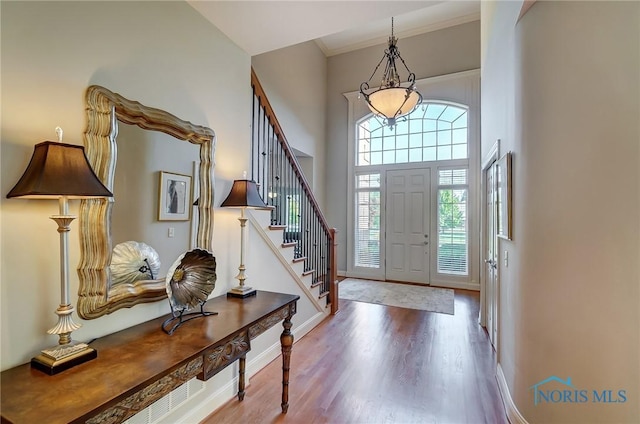 foyer entrance with crown molding, a towering ceiling, wood finished floors, baseboards, and stairs