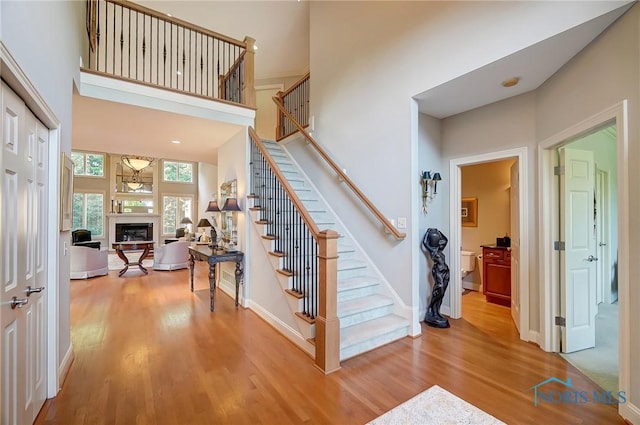entrance foyer featuring a towering ceiling, light wood-style flooring, a fireplace, and stairway
