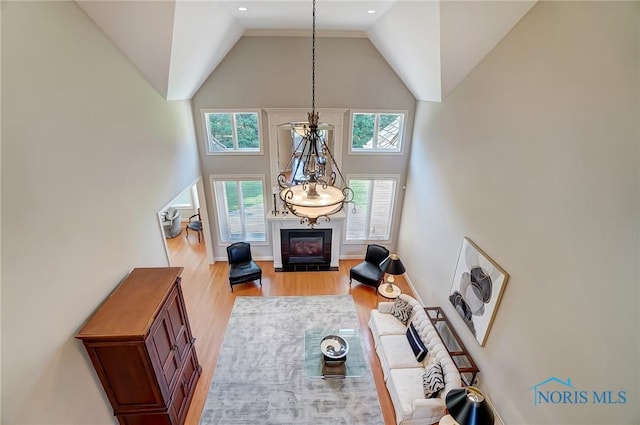 living area featuring a fireplace with flush hearth, light wood-type flooring, and high vaulted ceiling