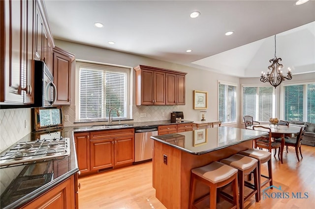 kitchen with decorative light fixtures, stainless steel appliances, brown cabinetry, a kitchen island, and a sink