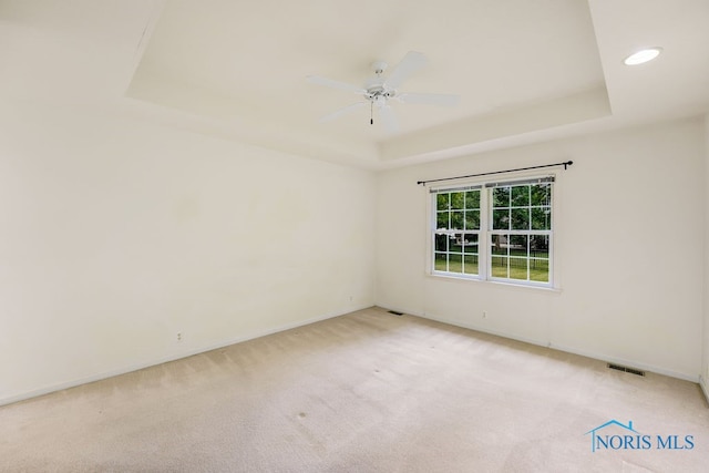 carpeted empty room with ceiling fan and a tray ceiling