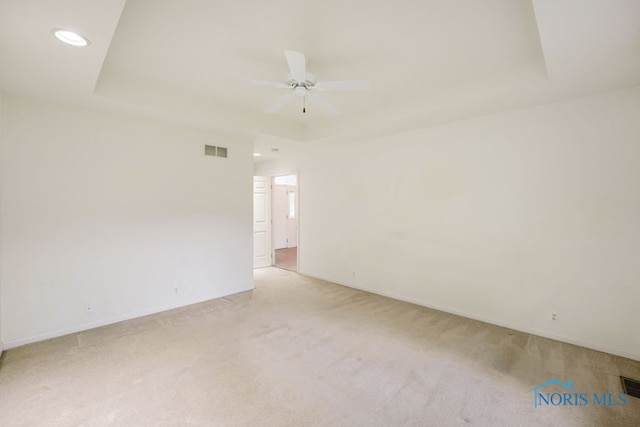 empty room featuring ceiling fan, a raised ceiling, and light carpet