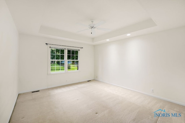 unfurnished room featuring a tray ceiling, ceiling fan, and light colored carpet