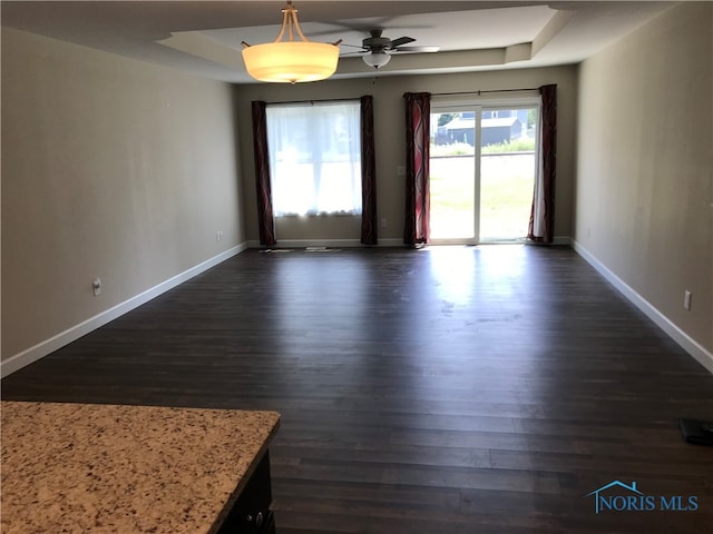 spare room with a tray ceiling, ceiling fan, and dark wood-type flooring