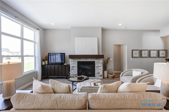 living room with a wealth of natural light, a stone fireplace, and wood-type flooring