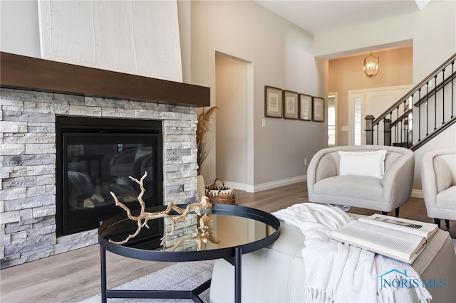 living room featuring a stone fireplace, a chandelier, and wood-type flooring