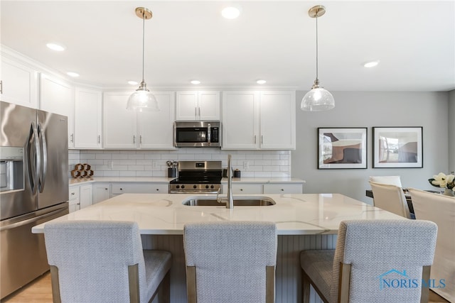 kitchen featuring appliances with stainless steel finishes, white cabinetry, decorative light fixtures, light stone counters, and a center island with sink