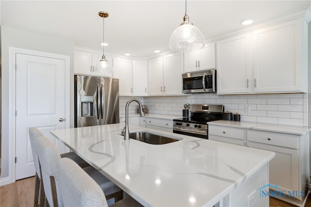 kitchen with white cabinets, a center island with sink, appliances with stainless steel finishes, pendant lighting, and sink