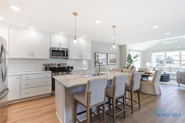 kitchen with a center island with sink, appliances with stainless steel finishes, light wood-type flooring, pendant lighting, and sink