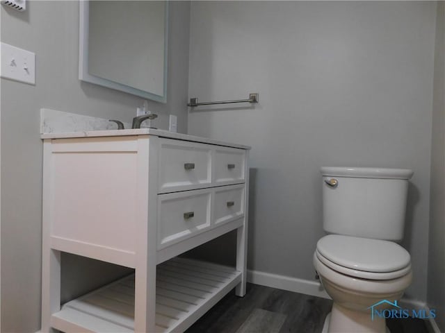 half bathroom with vanity, toilet, wood finished floors, and baseboards