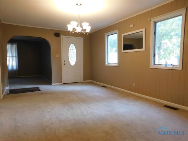 carpeted foyer entrance with crown molding and an inviting chandelier