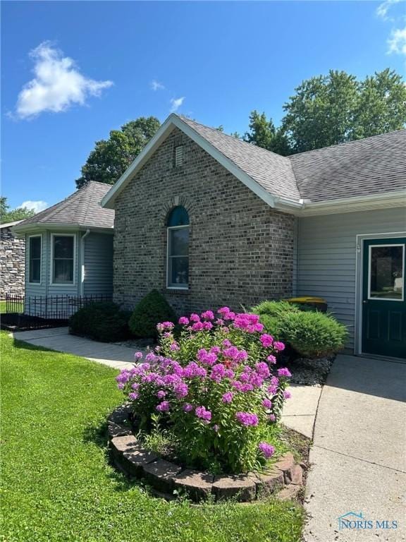 exterior space with a lawn, brick siding, and roof with shingles