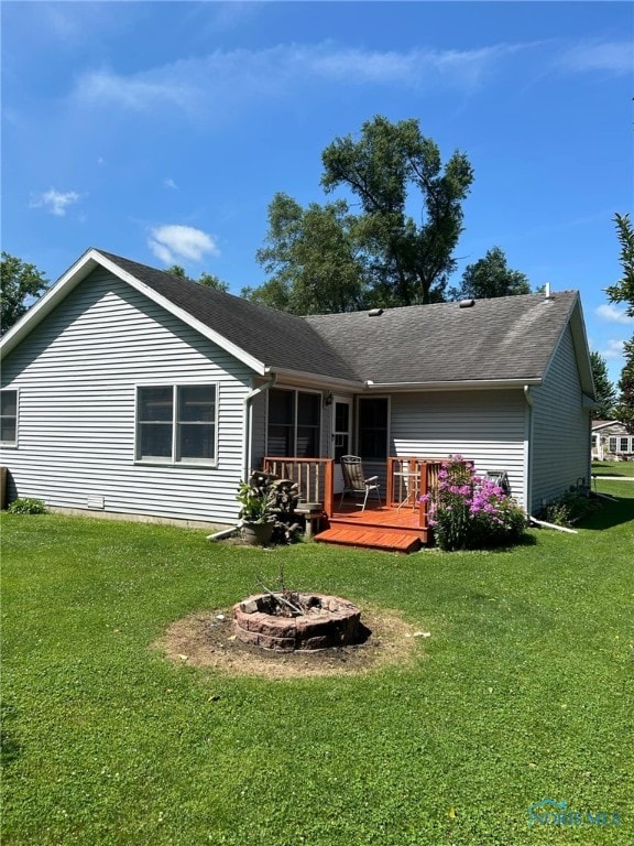 back of house with a wooden deck, an outdoor fire pit, and a lawn