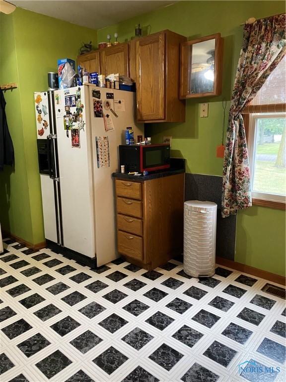 kitchen featuring glass insert cabinets, brown cabinets, dark countertops, and white refrigerator with ice dispenser