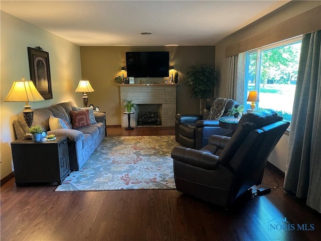 living room with a stone fireplace and dark wood-type flooring