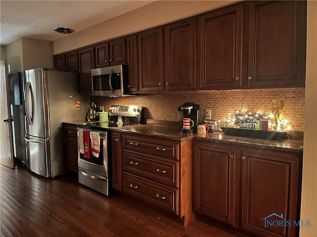 kitchen with tasteful backsplash, dark stone countertops, dark wood-type flooring, and appliances with stainless steel finishes