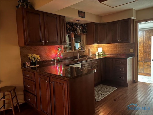 kitchen featuring backsplash, dark wood-type flooring, sink, hanging light fixtures, and kitchen peninsula