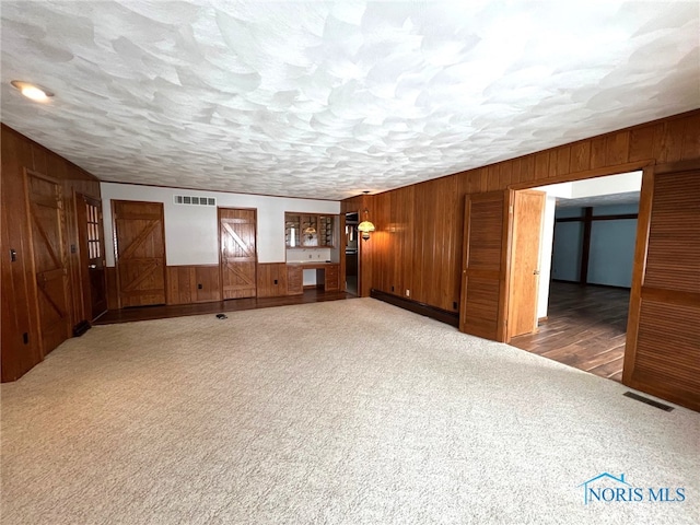 unfurnished living room with baseboard heating, wood walls, a textured ceiling, and dark colored carpet