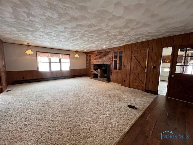 unfurnished living room with a baseboard radiator, a textured ceiling, a fireplace, and wood walls