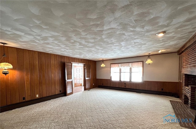 unfurnished living room with baseboard heating, carpet floors, a brick fireplace, and wood walls