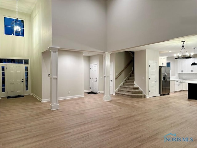 entryway featuring a high ceiling, light hardwood / wood-style floors, a chandelier, and ornate columns