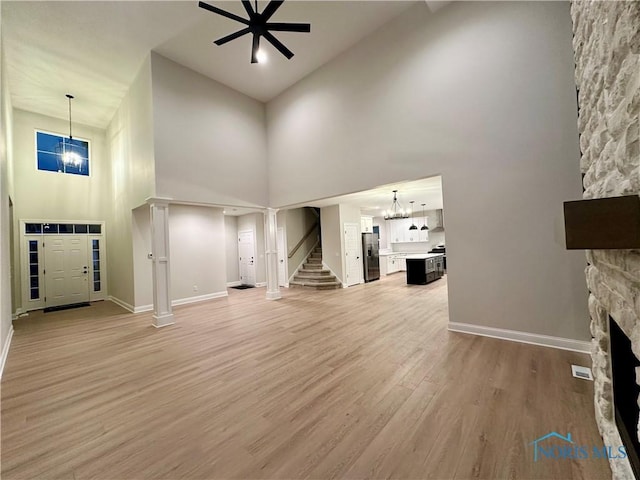 unfurnished living room with ceiling fan with notable chandelier, a fireplace, wood-type flooring, and a high ceiling