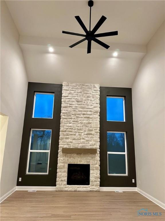 unfurnished living room with ceiling fan, a stone fireplace, high vaulted ceiling, and light wood-type flooring