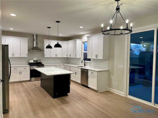 kitchen featuring sink, stainless steel appliances, a kitchen island, decorative light fixtures, and wall chimney exhaust hood