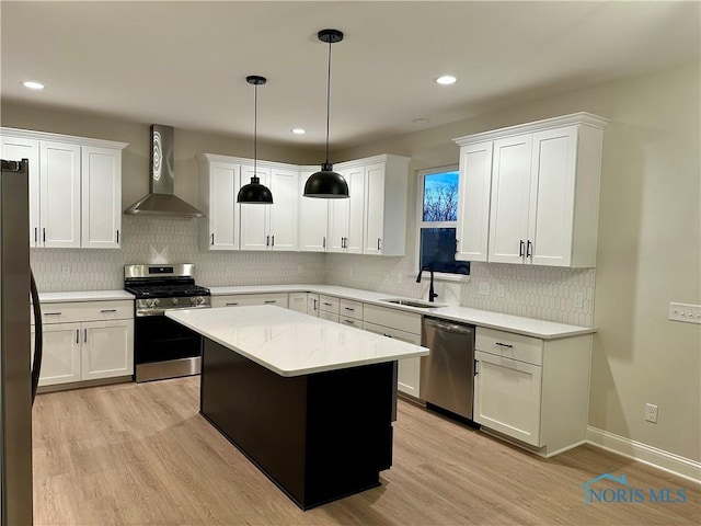 kitchen with wall chimney range hood, sink, stainless steel appliances, a center island, and decorative light fixtures