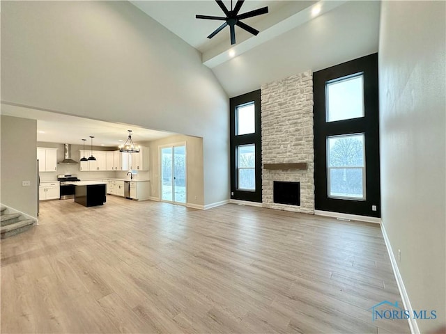 unfurnished living room featuring a fireplace, light wood-style floors, high vaulted ceiling, baseboards, and ceiling fan with notable chandelier