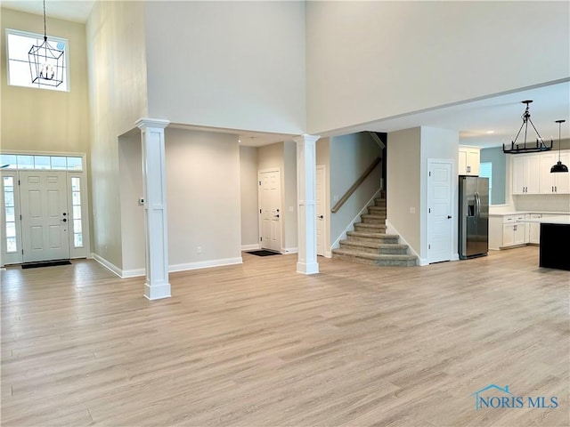 entryway with a high ceiling, light wood-type flooring, a chandelier, and ornate columns