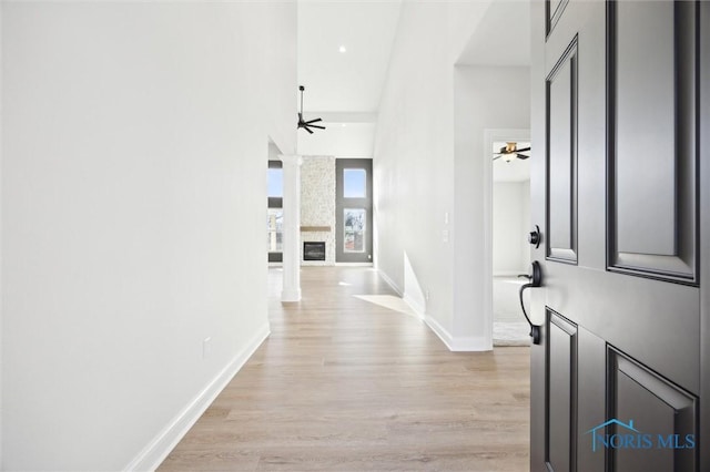 hallway featuring baseboards, light wood-style floors, a towering ceiling, and ornate columns