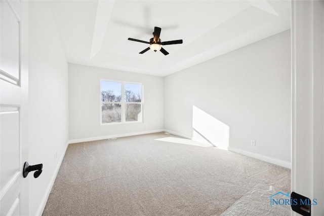 carpeted spare room with baseboards, a raised ceiling, and ceiling fan