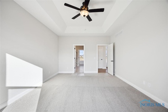 spare room featuring visible vents, a tray ceiling, baseboards, light colored carpet, and ceiling fan