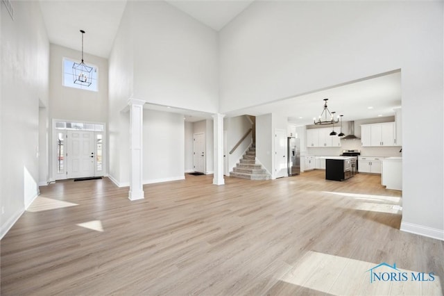 entrance foyer with light wood-type flooring, a notable chandelier, and decorative columns