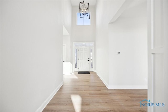 hallway with a chandelier, baseboards, light wood-style floors, and a towering ceiling